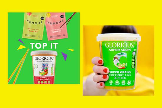 A hand with red nails holding a container of Glorious! super soups with a bright yellow background, and a colourful poster featuring soup packets to the left.