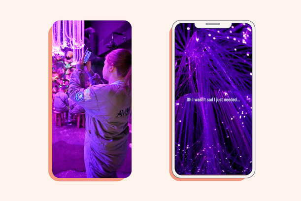 A person in a space suit takes a photo at a colourful, purple-lit exhibition, with an animated purple light display on a smartphone screen nearby.
