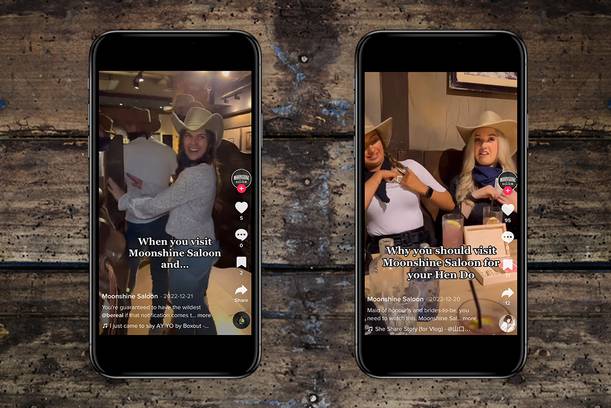 Two women in cowboy hats sitting at a table in a saloon, smiling and engaging with the camera, with social media posts about visiting Moonshine Saloon.