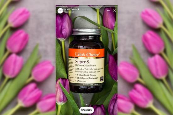Bottle of Udo's Choice Super 8 probiotic capsules surrounded by pink tulip flowers and green leaves, with a blurred background.
