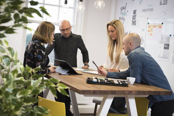 A group of five people collaborating around a wooden table in a bright meeting room.