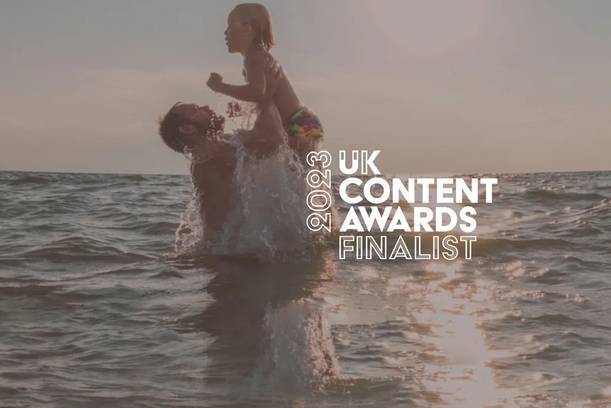 A person lifting a child in the ocean during sunset, with the text "2023 UK Content Awards Finalist" overlayed on the right side of the image.